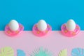 Three eggs in swimming pool floats and origami tropical leaves abstract on colorful background