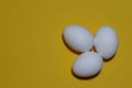 Three eggs, white on a yellow background, lay flat. Space for the text. Royalty Free Stock Photo