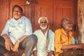 Three elderly indian man sitting outdoor past wooden door of city market