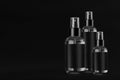 Three elegant tall, low transparent spray dispenser bottle for cosmetics with black label on black background, mock up, group.