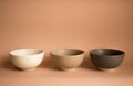 Three empty ceramic bowls - white, camel and gray, isolated on a dusty pink background.