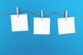 Three empty little sheets of paper hold by wooden clothespins on a string. Creative concept on a blue background and free copy Royalty Free Stock Photo