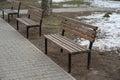 Three empty park benches in a spring park. Melting snow on the lawn in the background. No people. Daytime. Selective focus Royalty Free Stock Photo