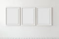 Three empty picture frames on the white wall. Triptych mockup