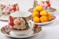 Three empty porcelain teacups with floral pattern and plate with wild apricots on a white tablecloth