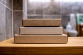 Three empty rectangular cardboard gift boxes stacked on a wooden surface with a blurred tiled background in soft natural light Royalty Free Stock Photo