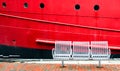 Three empty seats on a wharf next to a large red ship