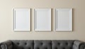 Three empty white frames on a beige wall above a gray tufted sofa. The scene is minimalistic and modern, ideal for Royalty Free Stock Photo