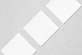 Three empty white square business card mockups lying diagonally on grey concrete background