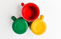 Three enameled cups in green, red and yellow colors on a white background.