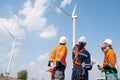 Three engineers or technician workers work together in front of cluster of windmill or wind turbine with blue sky and some cloud