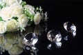 Three excellent diamonds of the first water and bouquet of white roses with reflection on black mirror background close up view. Royalty Free Stock Photo