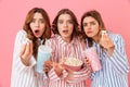 Three fascinating girls in homewear eating pop corn and drinking