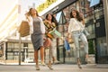 Three fashionable young women strolling with shopping bags. Satisfied women jumping on street.