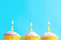 Three festive cupcakes in paper cups with yellow candles with flame for birthday on blue background copy space greeting card Royalty Free Stock Photo