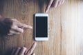 Three fingers of business man pointing at mockup of white mobile phone with blank black screen on vintage wooden table Royalty Free Stock Photo