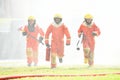 Three firefighters in uniform walking forward holding a fire extinguish tools surround with water drops and spray