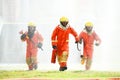 Three firefighters in uniform walking forward holding a fire extinguish tools surround with water drops and spray Royalty Free Stock Photo