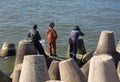 Three fishermen are fishing from concrete slabs of breakwaters by the sea Royalty Free Stock Photo