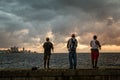 Three fishermen at the sunset lights standing on the Malecon street with sea and city in the background