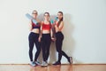 Three fitness young girls in sportswear standing against wall in fitness gym. Girls smiling and looking to camera. Royalty Free Stock Photo