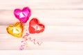 three foil metallic heart-shaped balloons in rose gold and red colors with interlaced ribbons on a beige and pink wooden