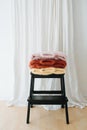 Three folded multi-colored sweaters lie on stepping stool in front of a curtain