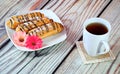 Three fresh eclairs decorated with flower buds and chocolate on a plate stand next to a white high mug of tea