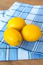 three fresh lemons on a wooden table. there is a cotton kitchen towel next to it