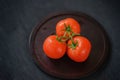 Three fresh red ripe tomatoes with water drops on branches, wooden plate, black background. Selective focus. Top view Royalty Free Stock Photo