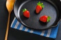 Three fresh red strawberries on black cast-iron pan served with wooden spoon and napkin. Concept Royalty Free Stock Photo