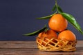 Three fresh ripe mandarin orange tangerine with green leaves in a woven wicker basket isolated on a wooden table Royalty Free Stock Photo