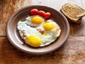 Three fried eggs with bacon on brown ceramic plate