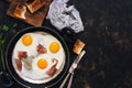 Three fried eggs with bacon in a frying pan with toast, dark rustic background. Top view, space for text. Royalty Free Stock Photo