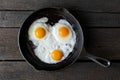 Three fried eggs in cast iron frying pan isolated on dark painted wood from above.