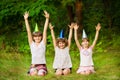 Three friendly children in festive cone caps, sit on grass, have fun together as celebrate birthday Royalty Free Stock Photo