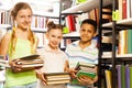 Three friends with books standing near bookshelf