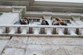 A candid shot of three diverse friends gazing into the sky from an ornate balcony, capturing a moment of curiosity and Royalty Free Stock Photo