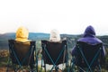 Three friends sit in camping chairs on top of a mountain, travelers enjoy nature and cuddle, tourists look into distance on back Royalty Free Stock Photo