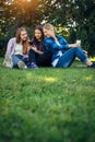 Three friends spend their free time sitting in the park on green lawn. Young pretty girls talking, smiling, looking photo Royalty Free Stock Photo