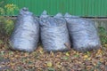 three full gray plastic bags with garbage stand on the ground near the wall