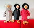 Three geese stuffed animals with weatherproof jackets sit on a red sofa in front of a white wall Royalty Free Stock Photo