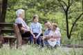 Three generation family in park: grandfather sitting on bench, father, and grandchildren