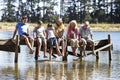 Three Generation Family Sitting On Wooden Jetty Looking Out Over Lake