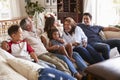 Three generation Hispanic family sitting on the sofa watching TV, grandmother using remote control Royalty Free Stock Photo