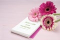 three gerbera flowers lying on a writing pad, pastel pink colored background with copy space, german text Royalty Free Stock Photo