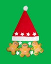 Three gingerbread men and a Santa Claus hat are located on a green background.