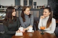 Three girlfriends in a cafe are talking and drinking their beverages