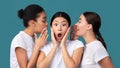 Three Girlfriends Sharing Secrets Standing On Turquoise Background In Studio Royalty Free Stock Photo