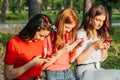 Three girls chatting with their smartphones at the park. Gen Z young girl friends using gadget and having fun outdoors